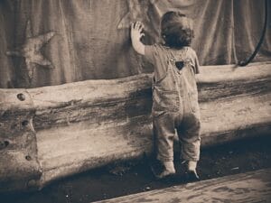 Toddler in jeans reaching up touching a hanging fabrick. Photo in sepia coloer