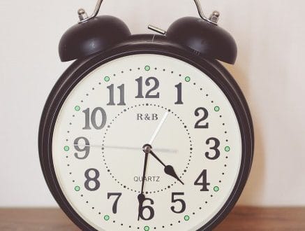 a black clock against a white wall on top of a wooden table