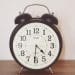 a black clock against a white wall on top of a wooden table