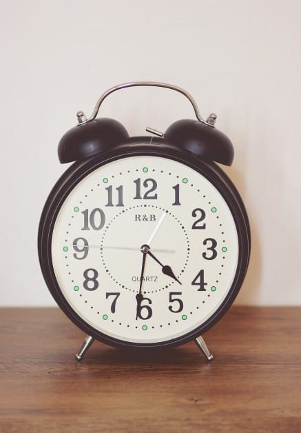 a black clock against a white wall on top of a wooden table